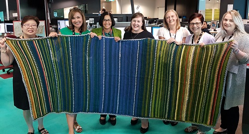Tess Davies (centre) and staff at the Bureau's Victoria Regional Forecasting Centre in Melbourne holding the weather blanket Tess knitted.