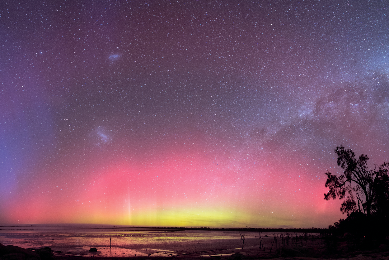 Green, pink and purple light in the night sky, reflected in the lake's waters below.