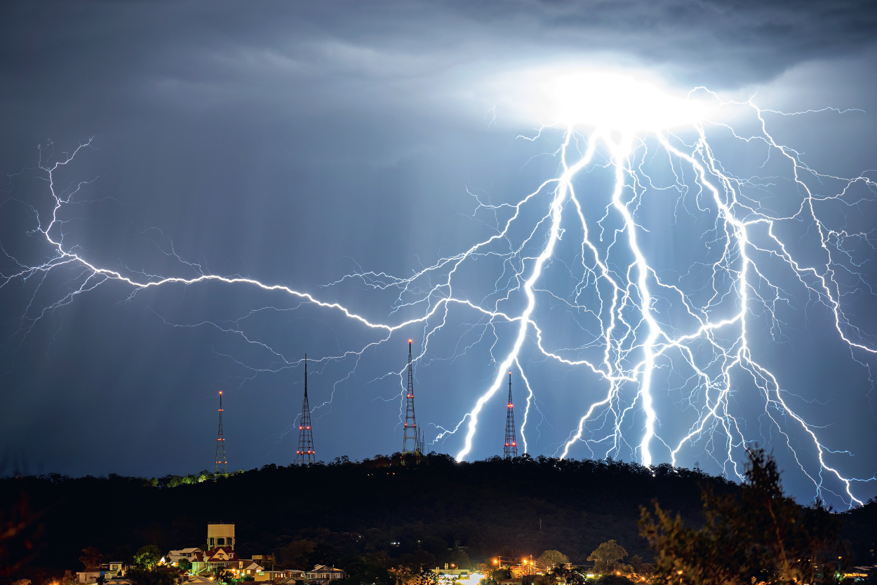 Many lightning strikes in the night sky over a mountain with transmission towers.