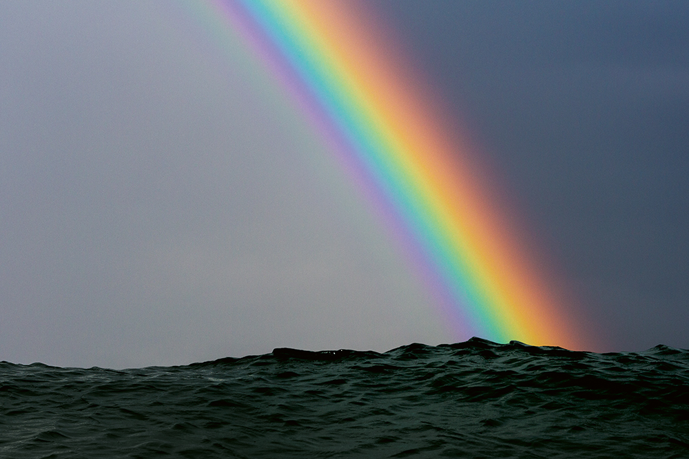 Vivid rainbow in a dark sky resting on top of slate-coloured sea.