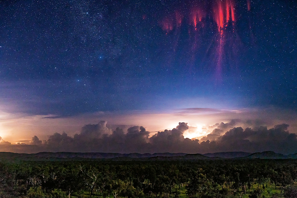 Red sprites flicker above a thunderstorm in a starry sky above Kununurra.