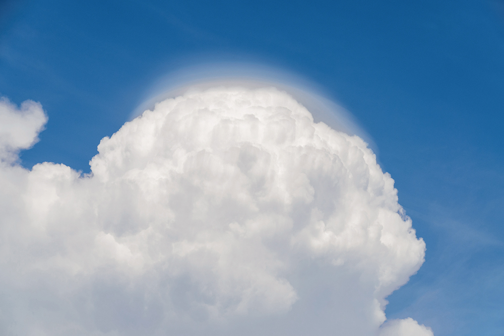 Billowing white cumulus cloud in blud sky with a 'cap' of wispy cloud at the top.