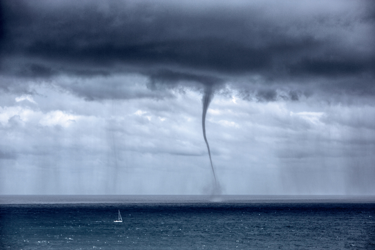 Waterspout dropping from grey clouds over the ocean, amid heavy rain.