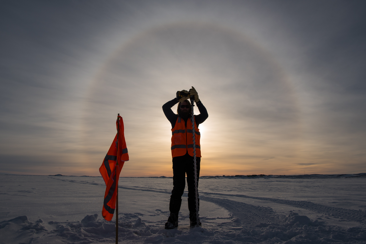 Image: An AAD staff member drills sea ice to measure its thickness, beneath a sun halo. Credit: Barry Becker