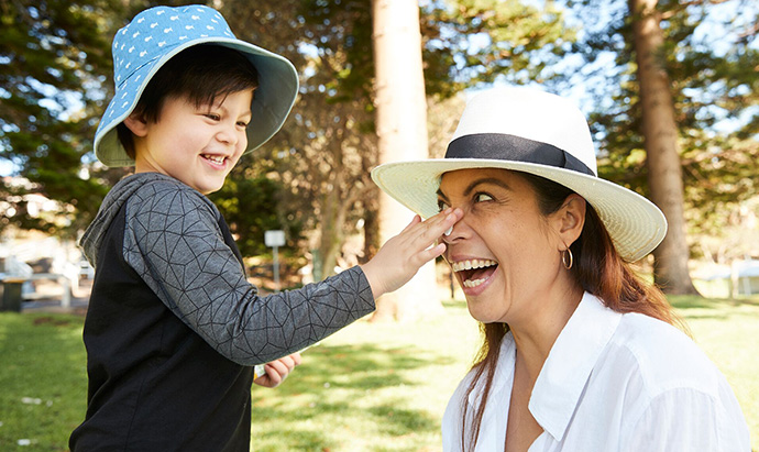 Toddler putting sunscreen on adult woman's face. Both are smiling happily.