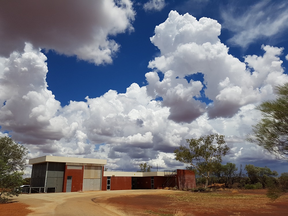 Tall, white cumulus clouds over trees and building in a rural setting