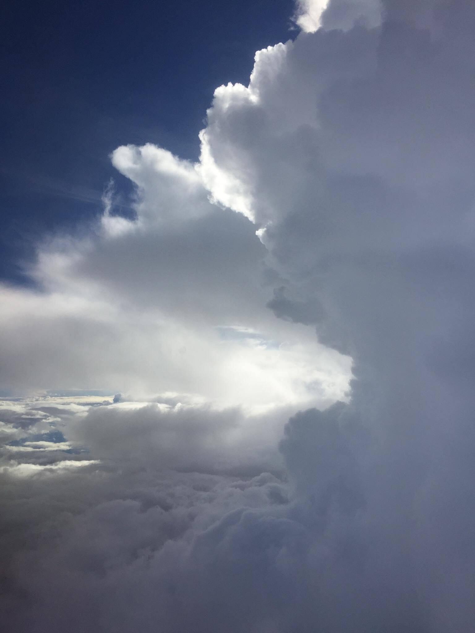 Photo taken above the clouds, showing a layer of cloud with fluffy clouds rising above it