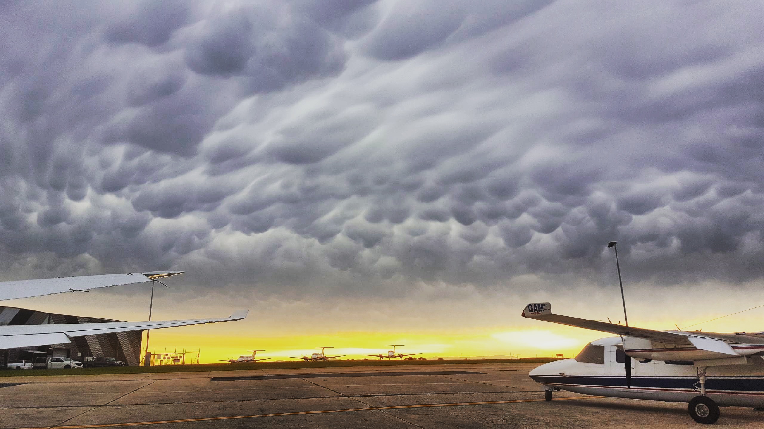 Storm clouds over planes on the tarmac at an airport.