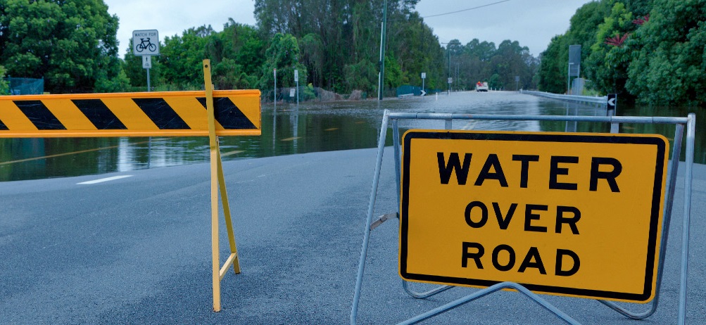Image: Sign warning of water over road, ahead of section of road underwater. Credit: SES NSW