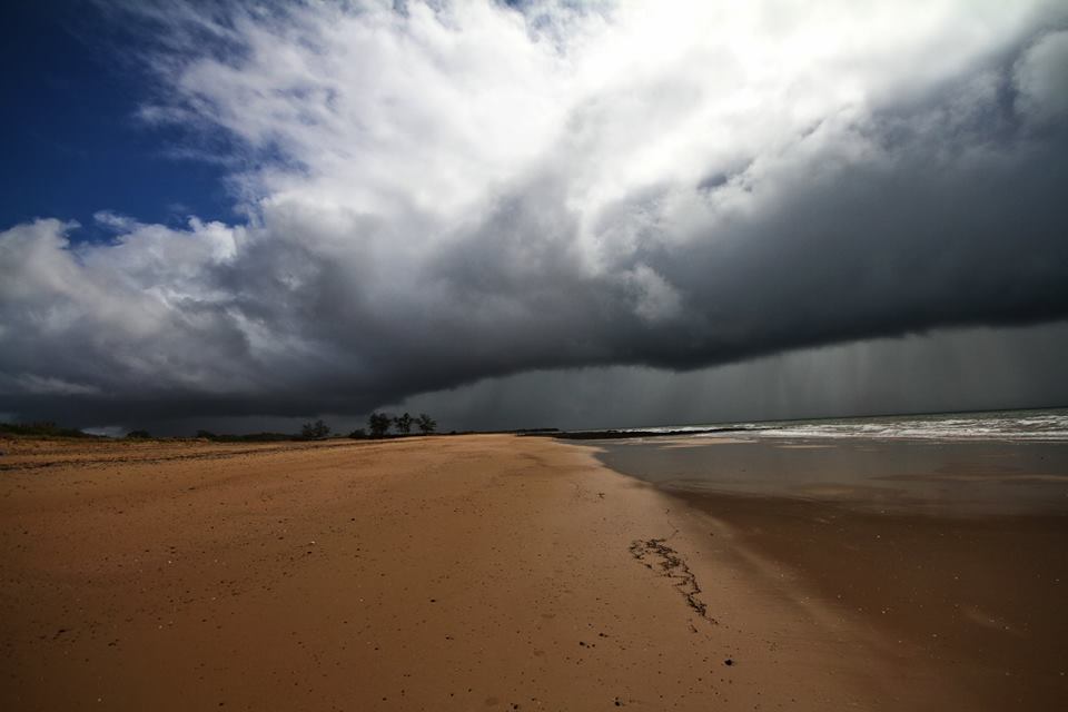Long grey cloud over an empty beach with rain falling in the sea.