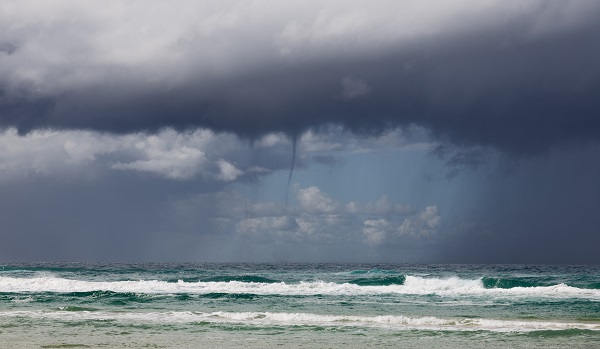 Waterspout emerging from grey clouds above ocean waves.