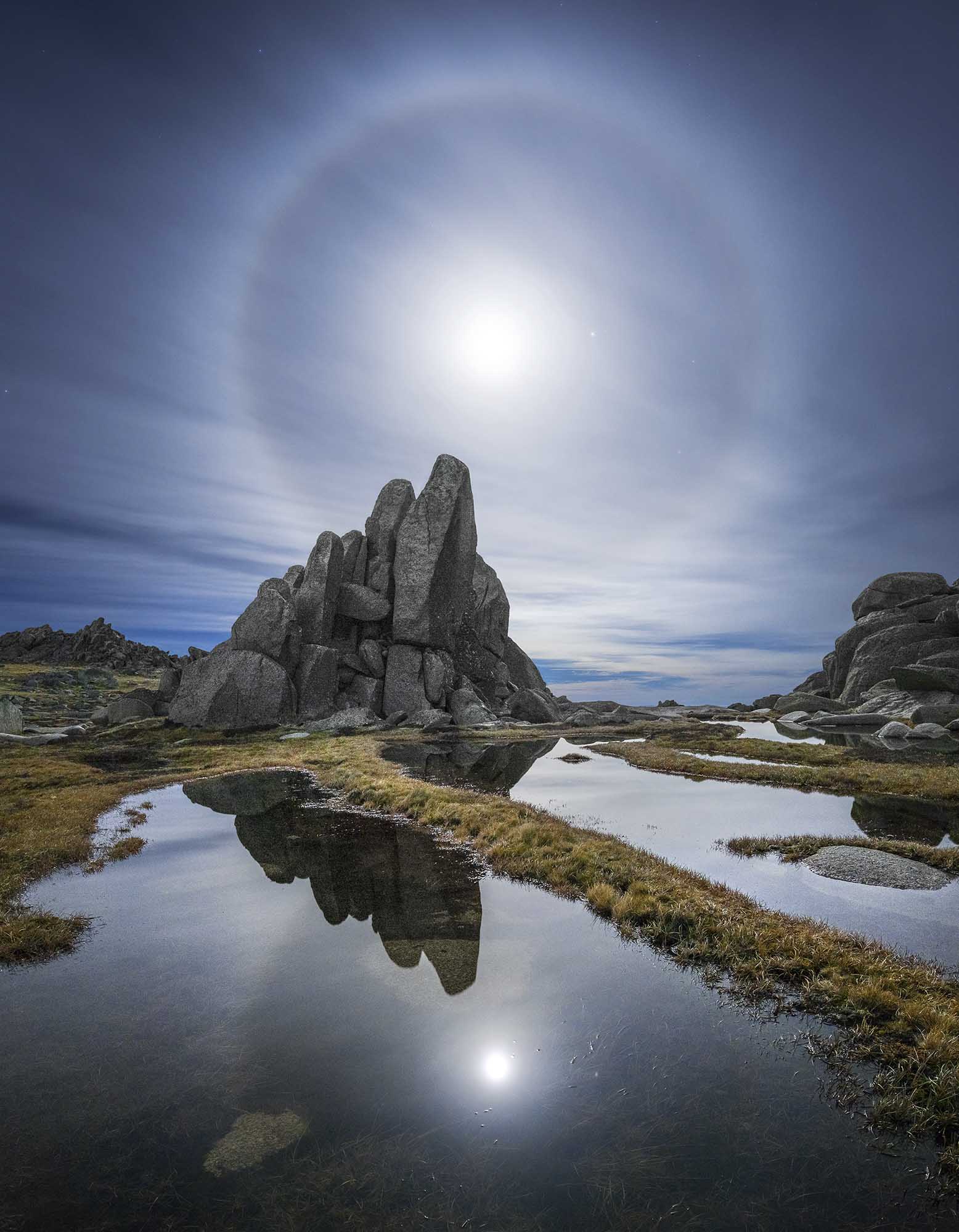 Moon halo shining over rock escarpment with reflective water in foreground
