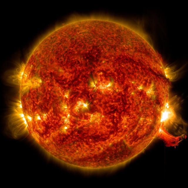 The sun as an orange globe, with patches of yellow light, including a bright solar flare.