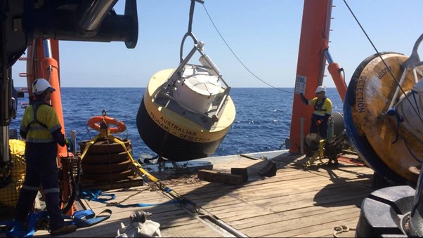 Large Australian tsunami detection buoy being launched into the sea from the deck of a ship.