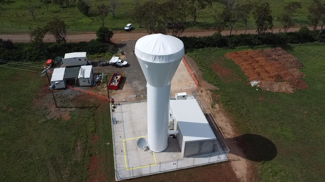 Looking down on a white radar tower on a concrete base in a grassy field.