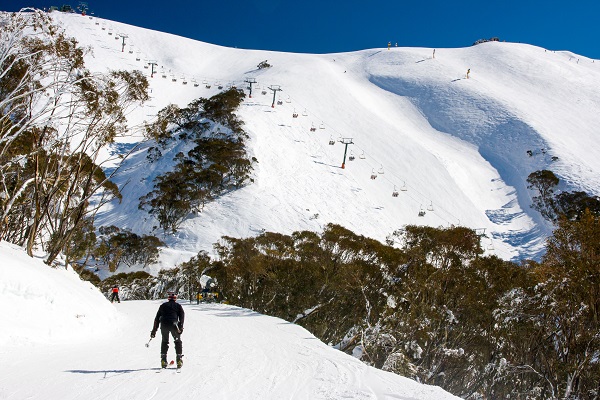 Skiers on a snowy mountain with a chairlift across the slopes in the background.